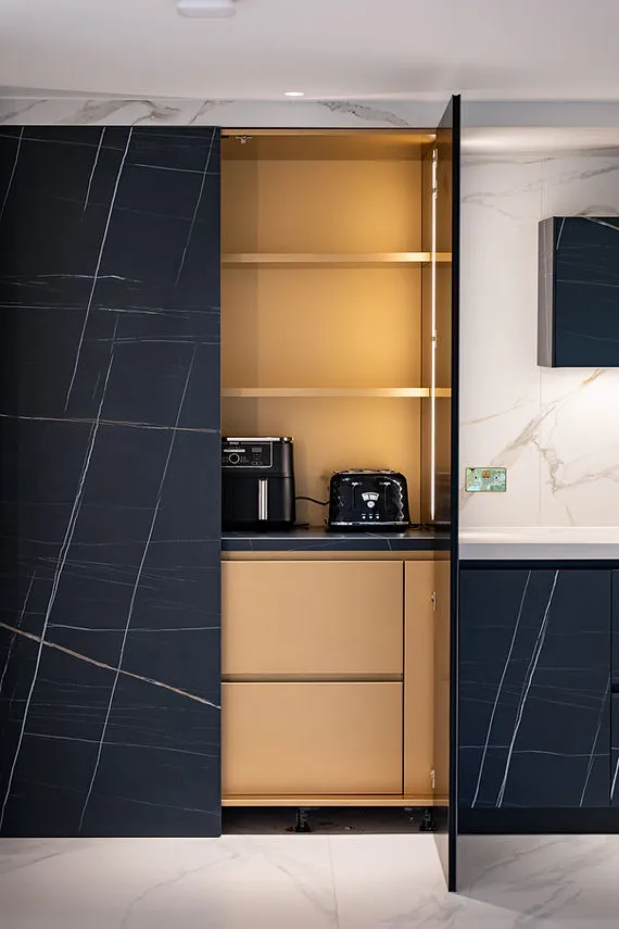Illuminated gold-toned shelving and appliances behind dark veined cabinet doors.
