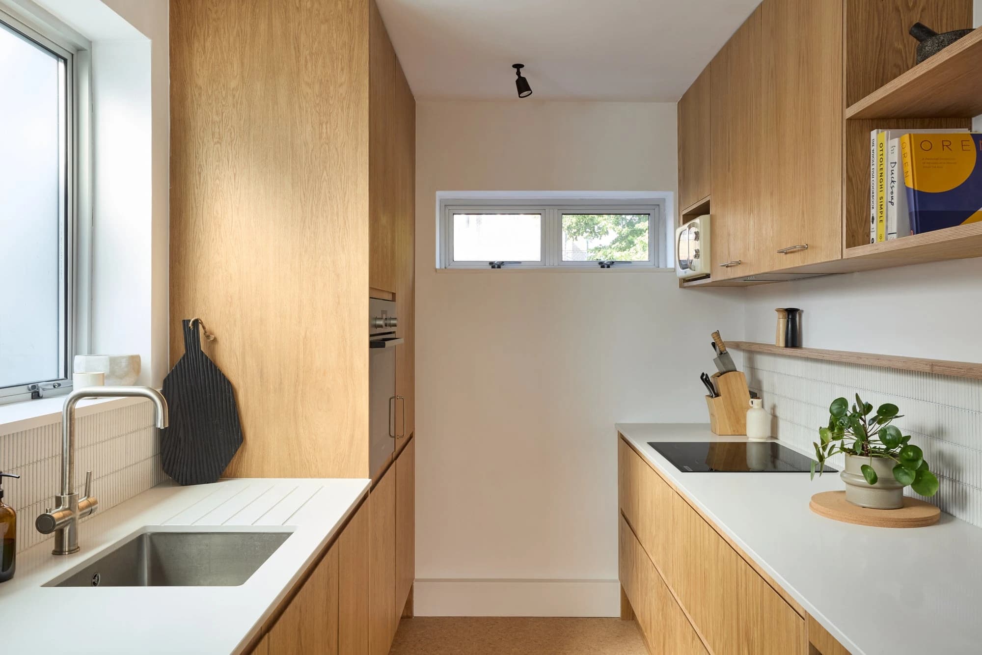 Narrow kitchen with oak cabinets, a white worktop and a window above the sink