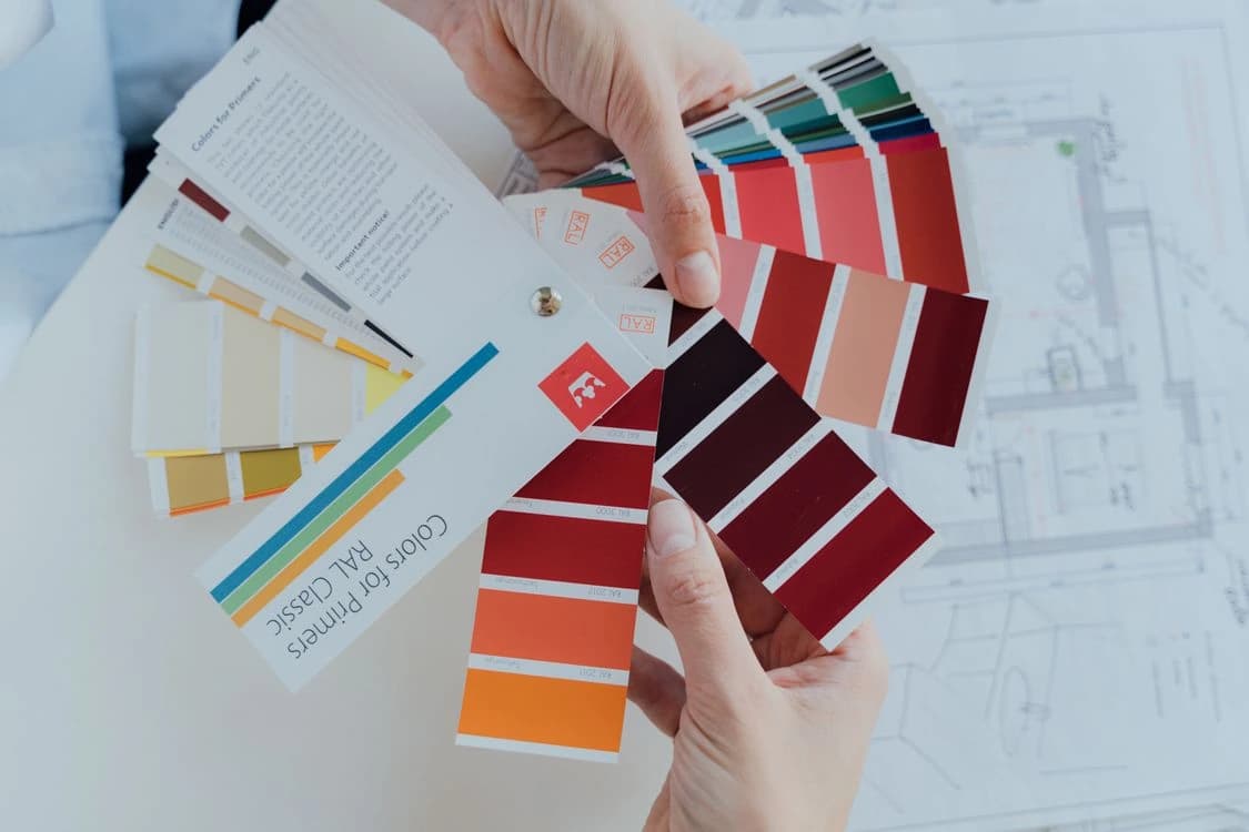 Hands comparing two colour fans over a printed plan