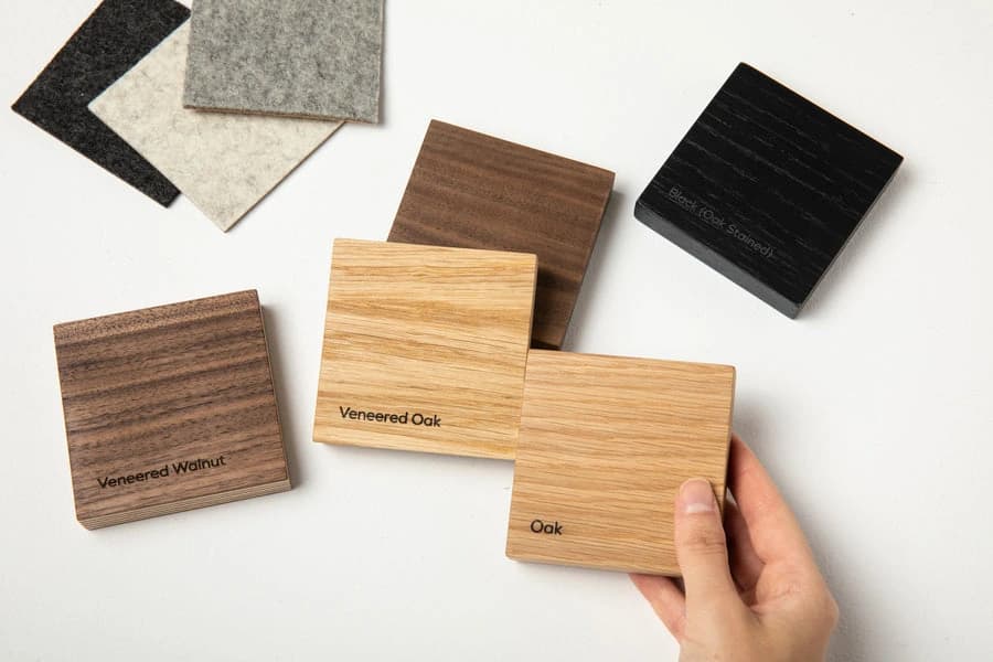 Hand holding labelled oak and walnut finish samples beside other material swatches