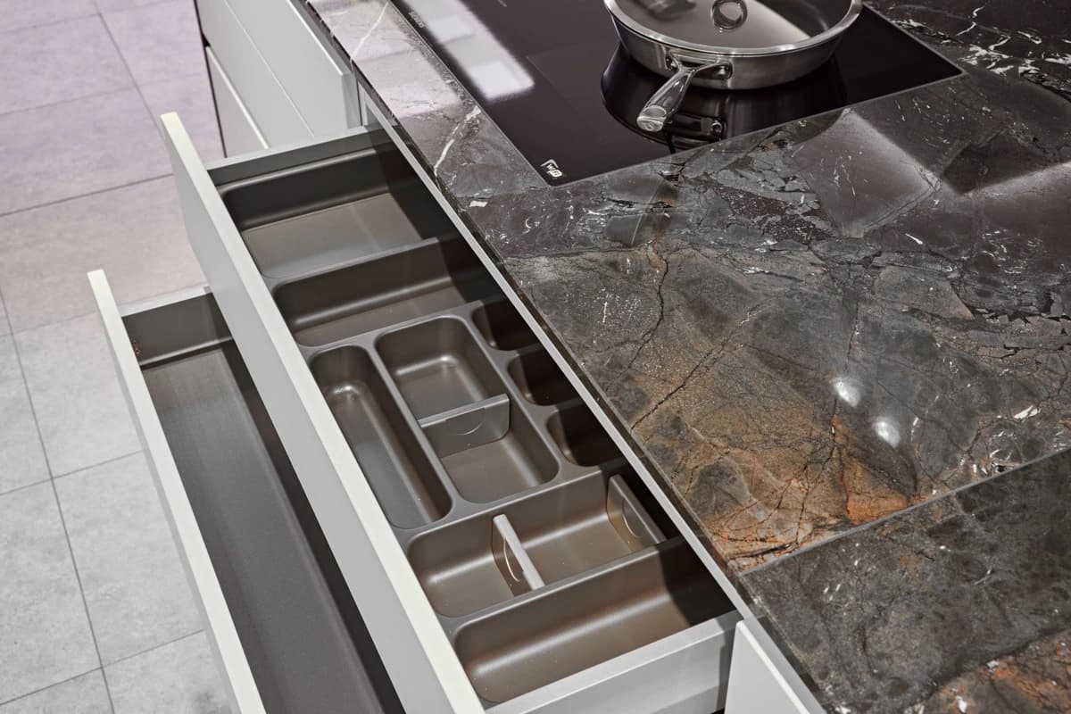Open kitchen drawers beneath a dark stone worktop and hob