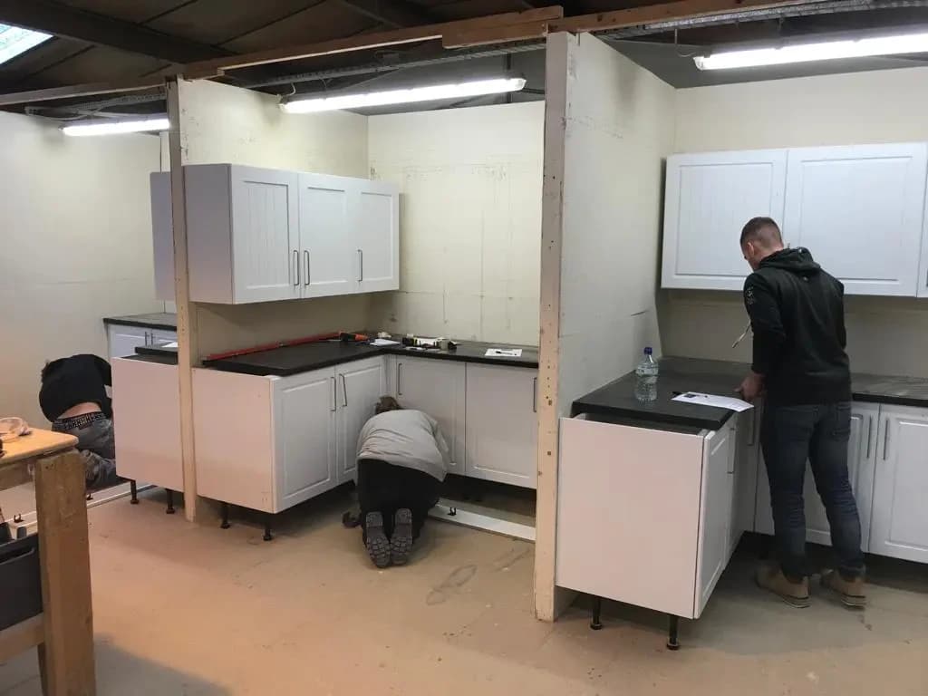 People fitting base cabinets in a workshop kitchen
