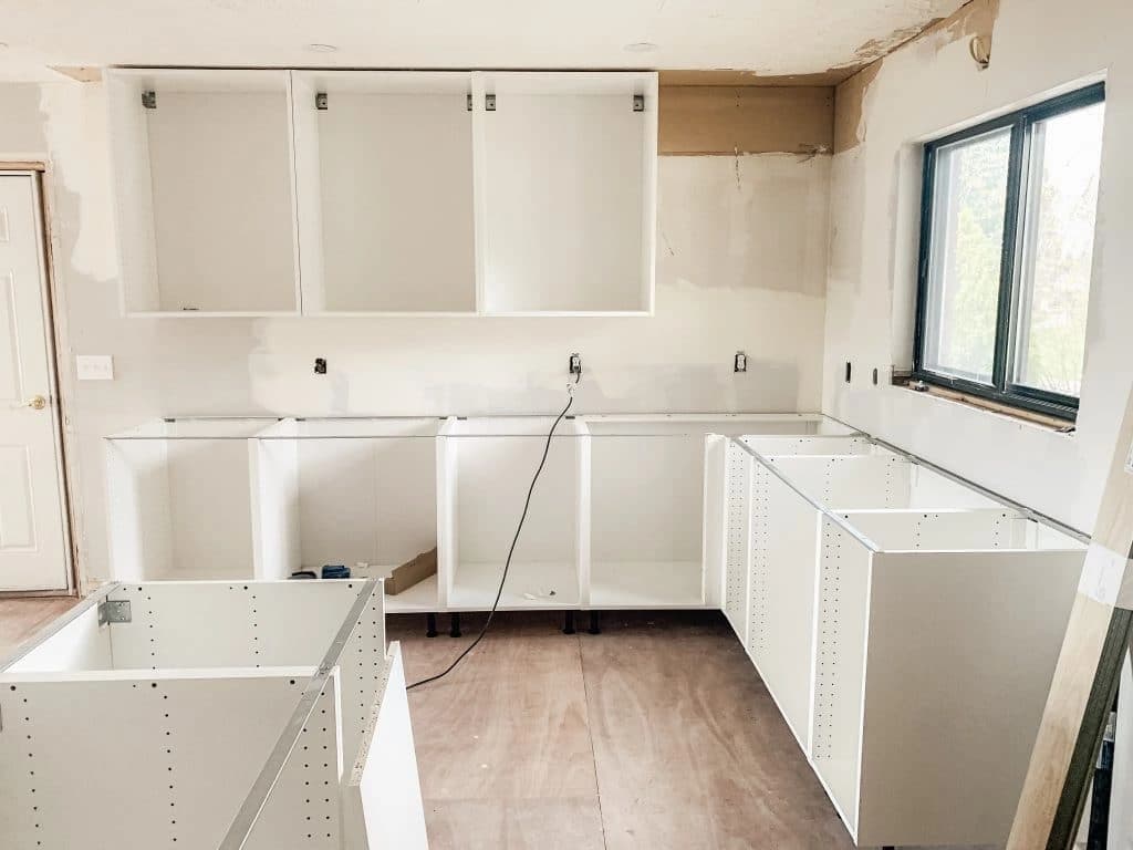 Partly installed white kitchen cabinets with an unfinished floor
