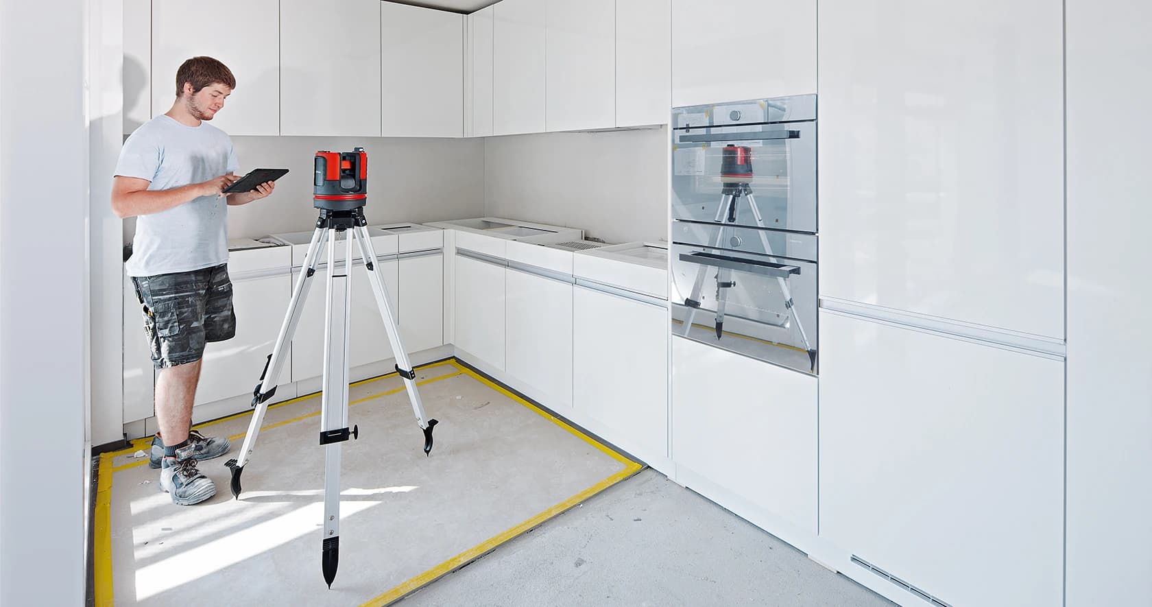 Person measuring a kitchen beside a tripod-mounted laser