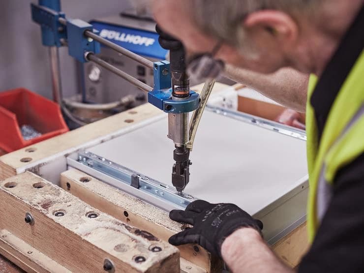 Worker drilling a cabinet component on a bench