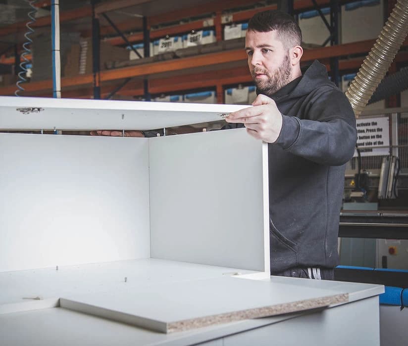Worker assembling a white cabinet in a workshop