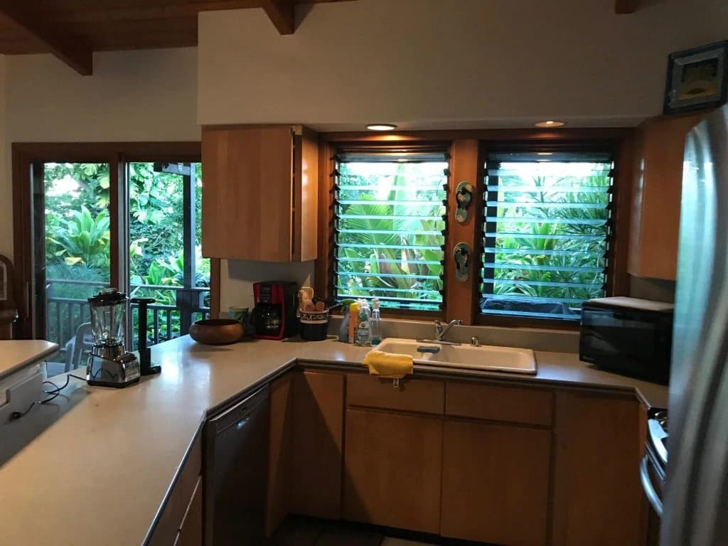 Timber kitchen cabinetry beside louvred windows and trees