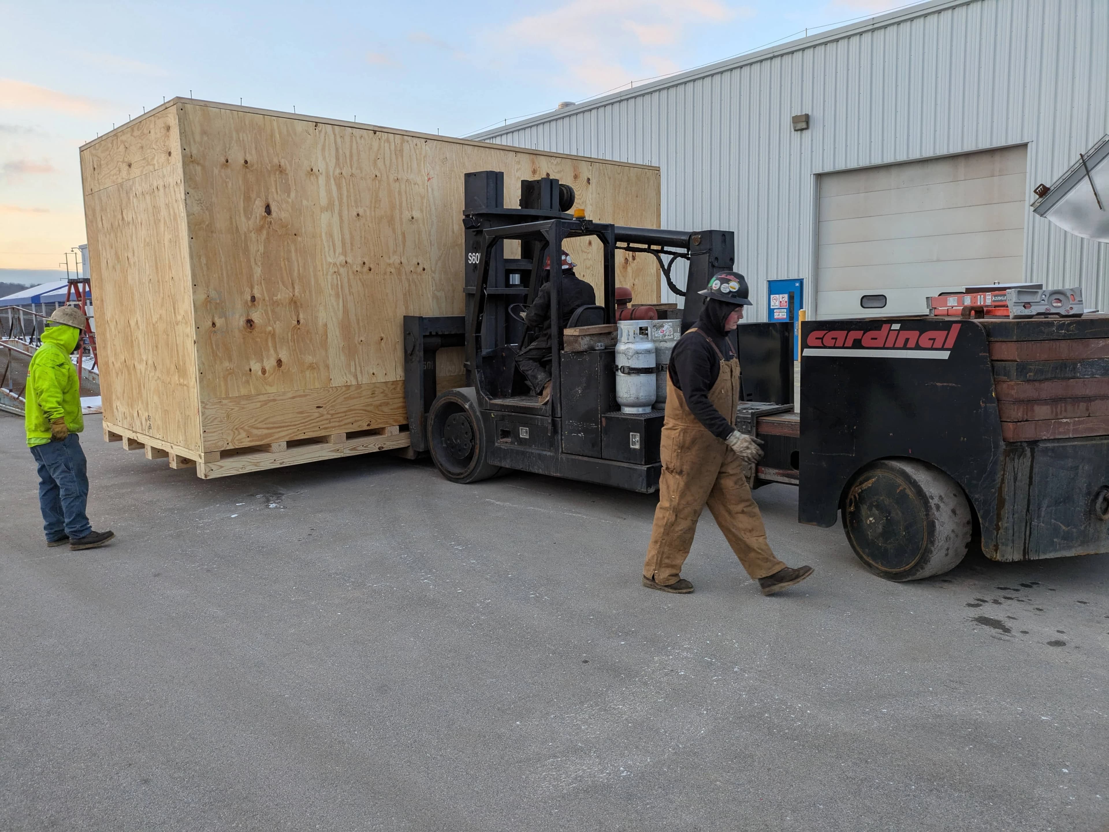 Forklift moving a large wooden shipping crate outside a warehouse