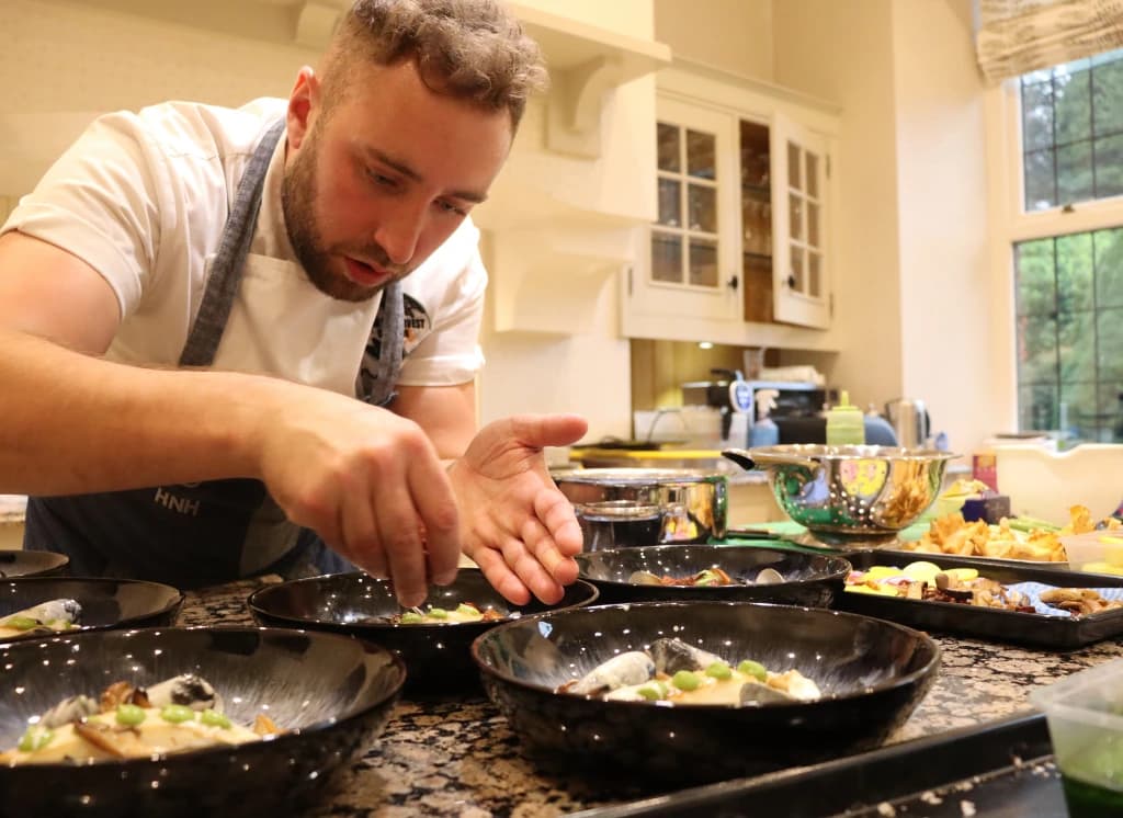 Cook plating food beside pans in a kitchen