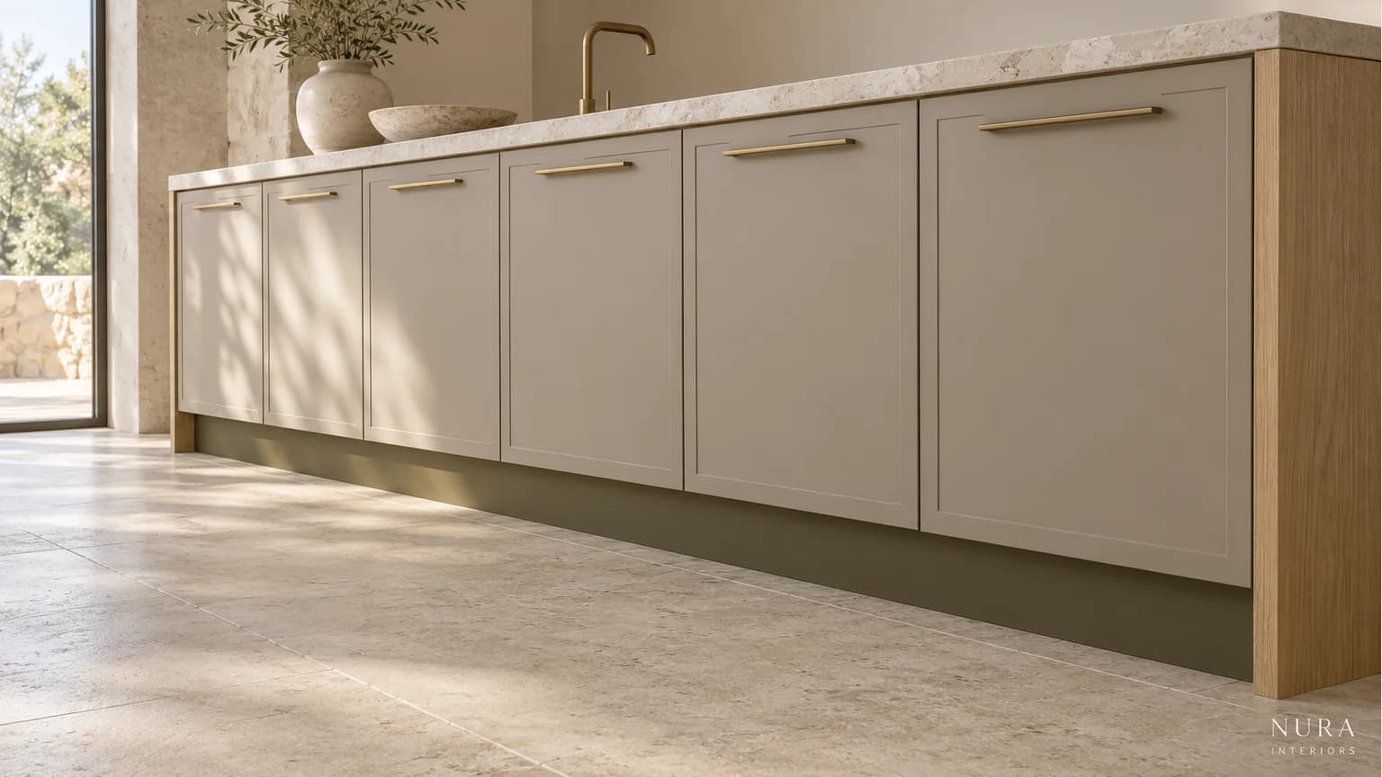 Recessed olive plinth beneath warm grey kitchen cabinets with an oak end panel and pale stone floor