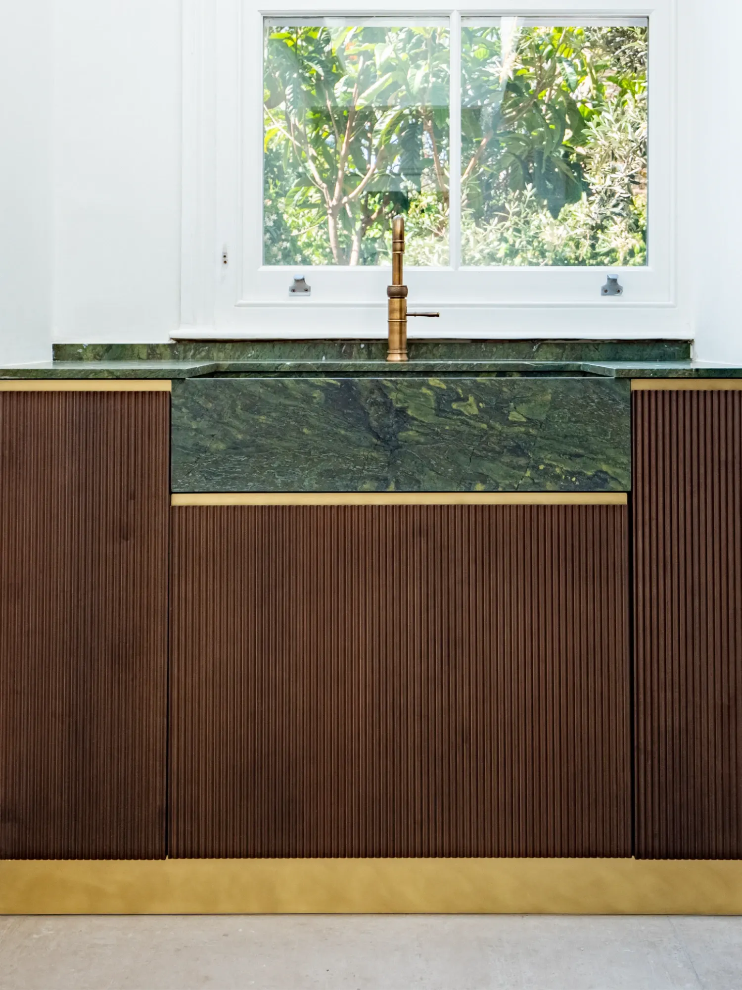 Warm timber kitchen with green stone worktop and garden view