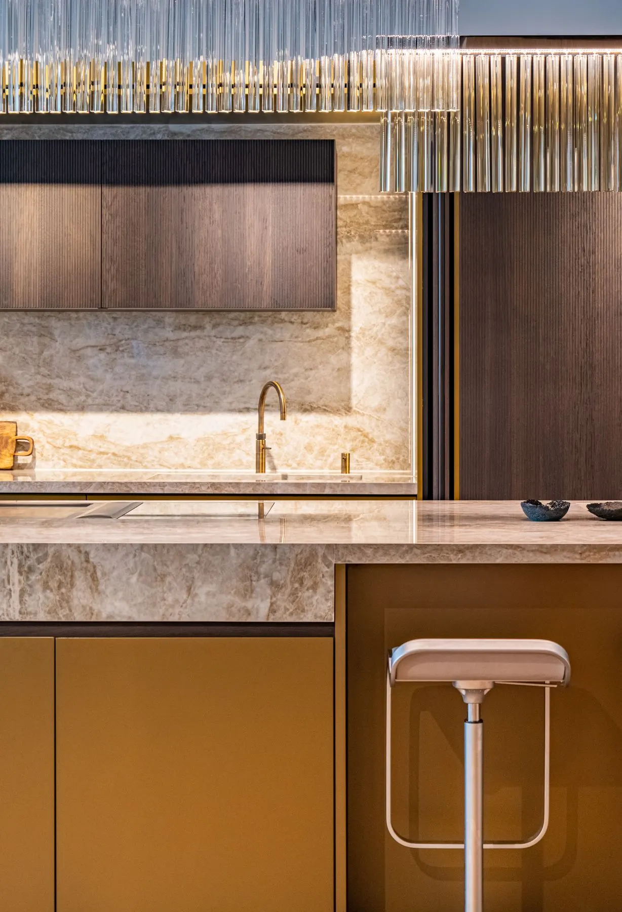 Bespoke kitchen with warm stone surfaces, ribbed timber cabinetry and a sculptural glass pendant light
